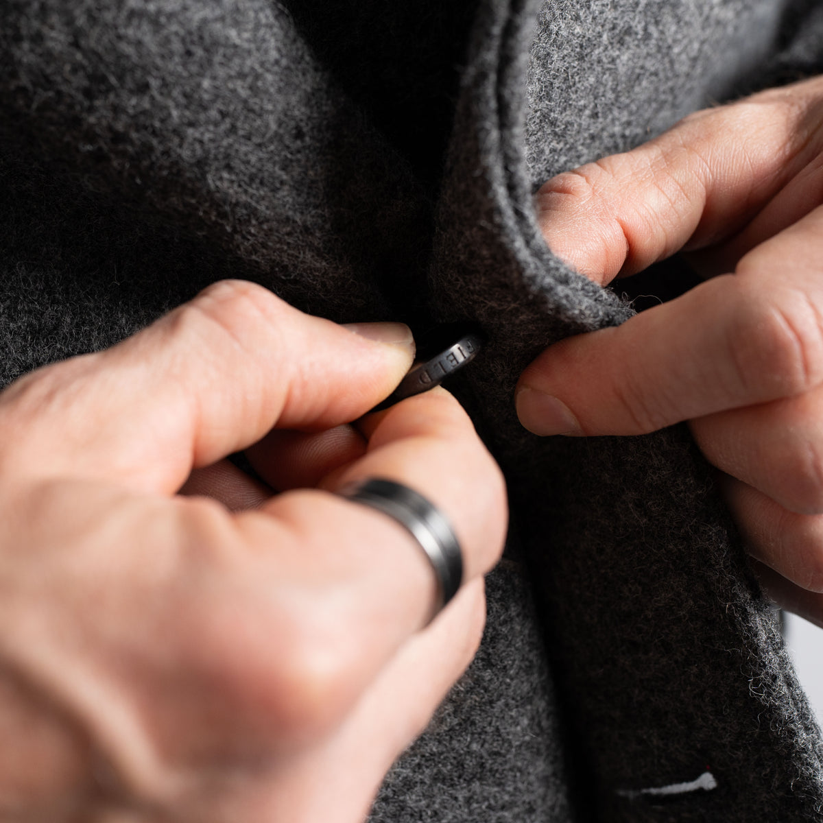 Close-up of hands buttoning a dark gray coat